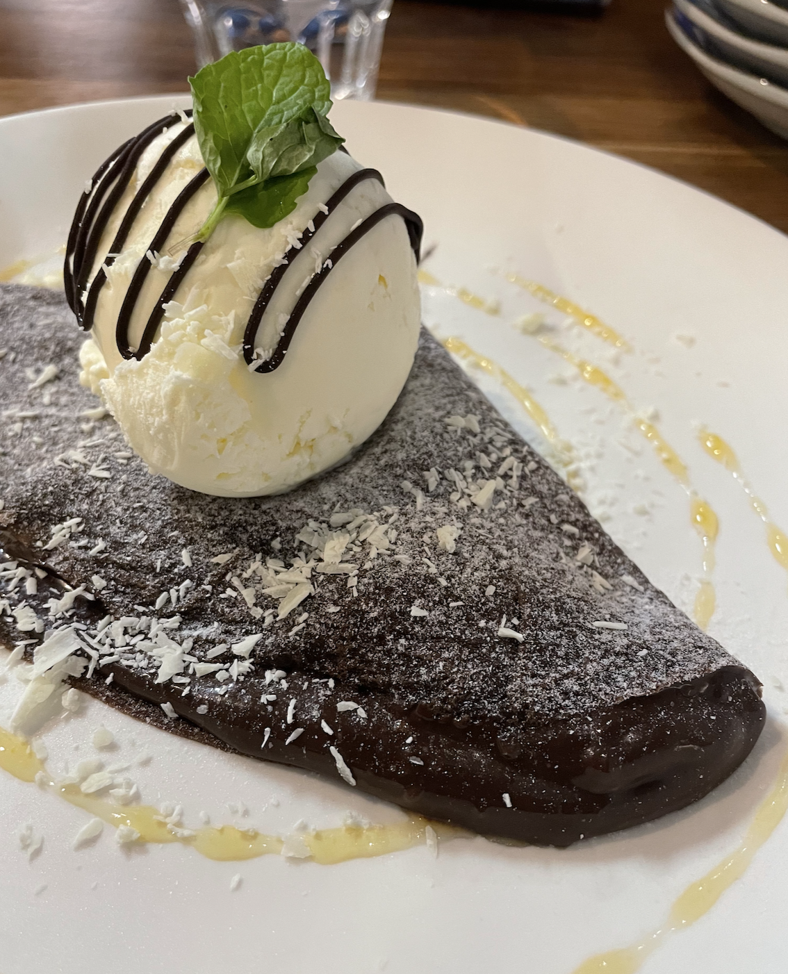 A photo of a chocolate crepe, stuffed with chocolate sauce and topped with vanilla ice cream.