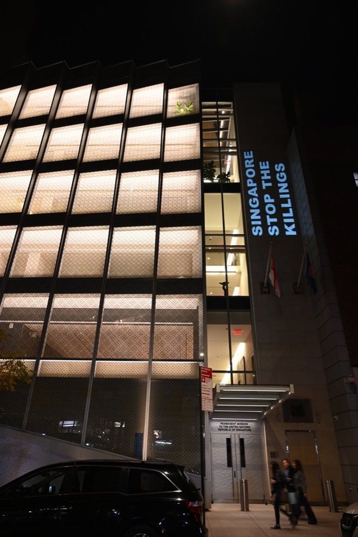 A photo of Singapore's Permanent Mission to the United Nations in New York City at night. The message "SINGAPORE: STOP THE KILLINGS" has been projected on to the building.