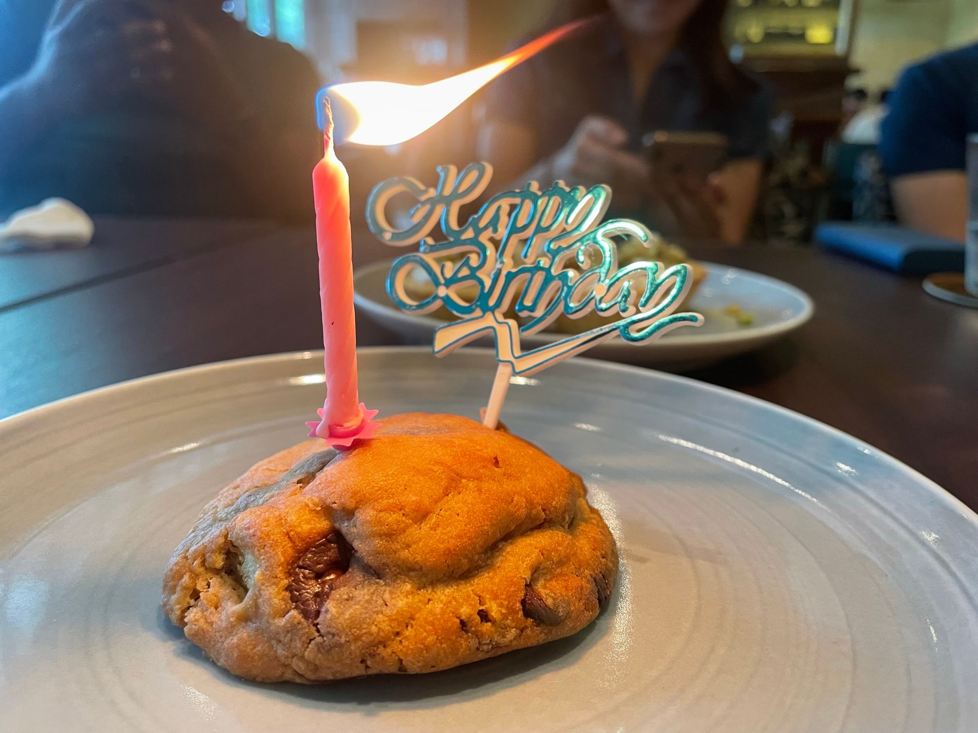 A chocolate chip cookie with a candle and a 'Happy Birthday' decoration stuck into it.