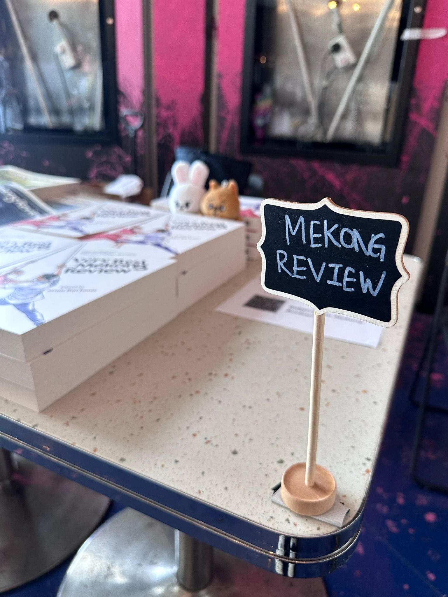 A metal table with books entitled "The Very Best of Mekong Review" arranged on them. In the foreground is a small stand on which "Mekong Review" is written.